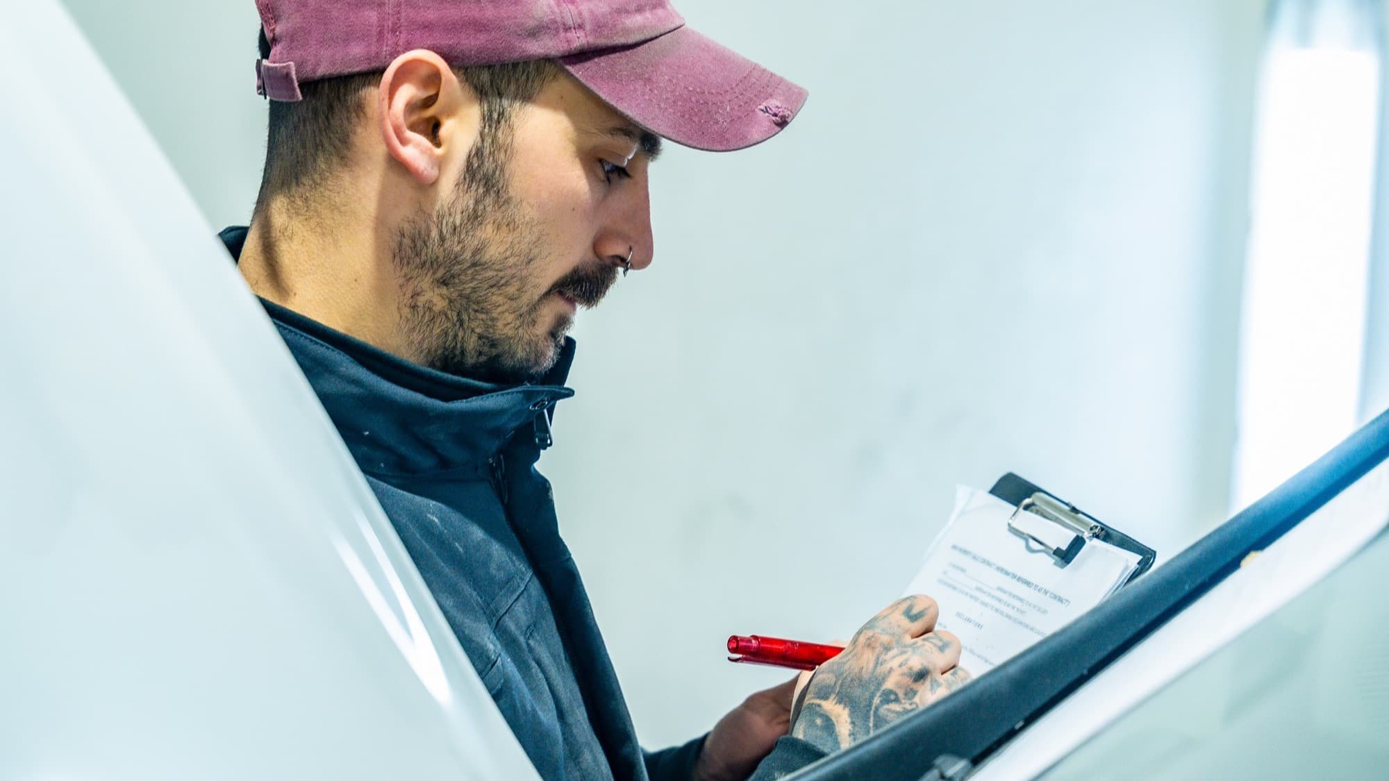 Worker inspects vehicle while holding clipboard.
