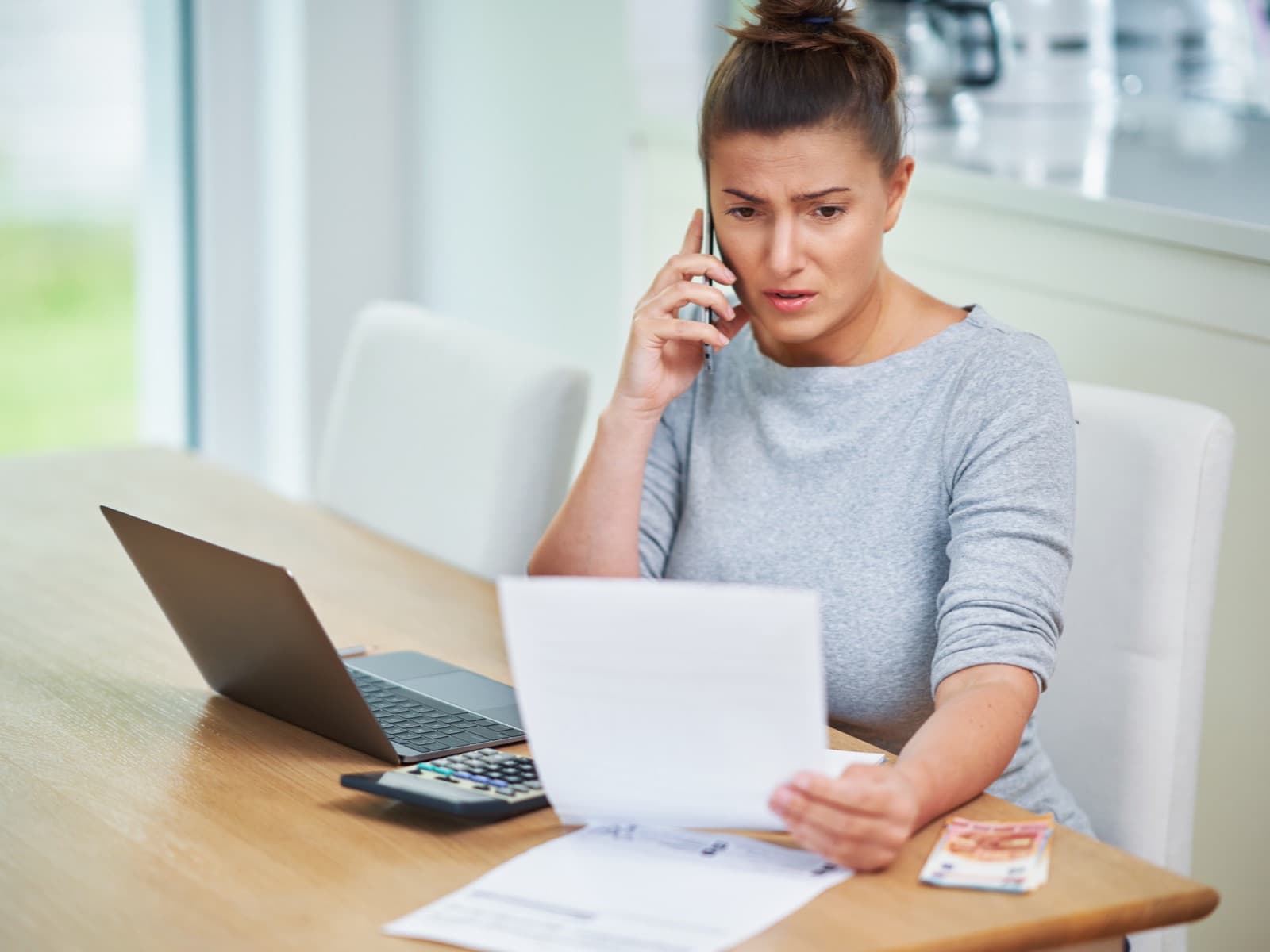 Worried woman on phone at desk with laptop.