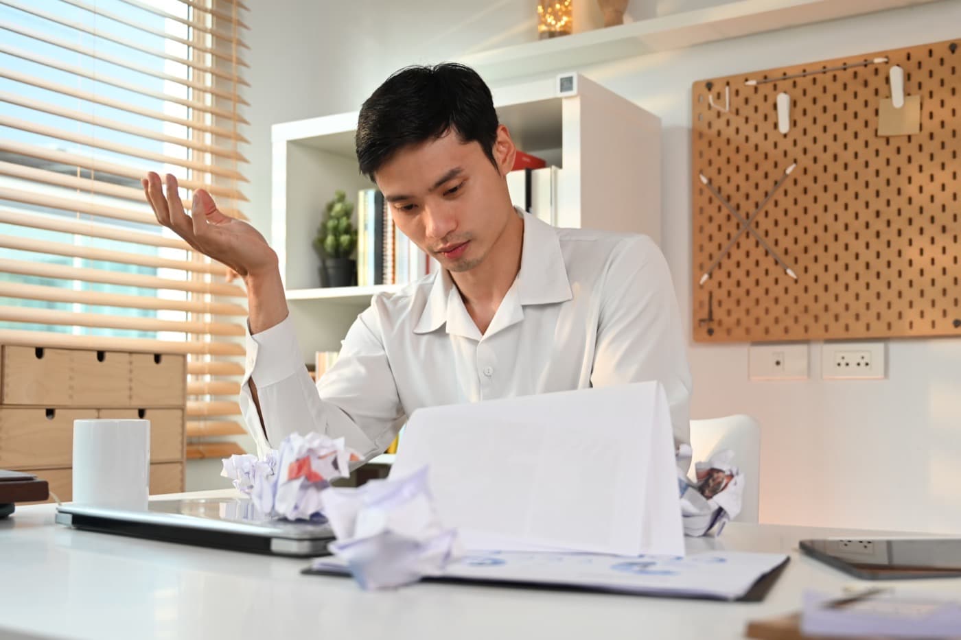 Frustrated man with wrinkled papers at desk.